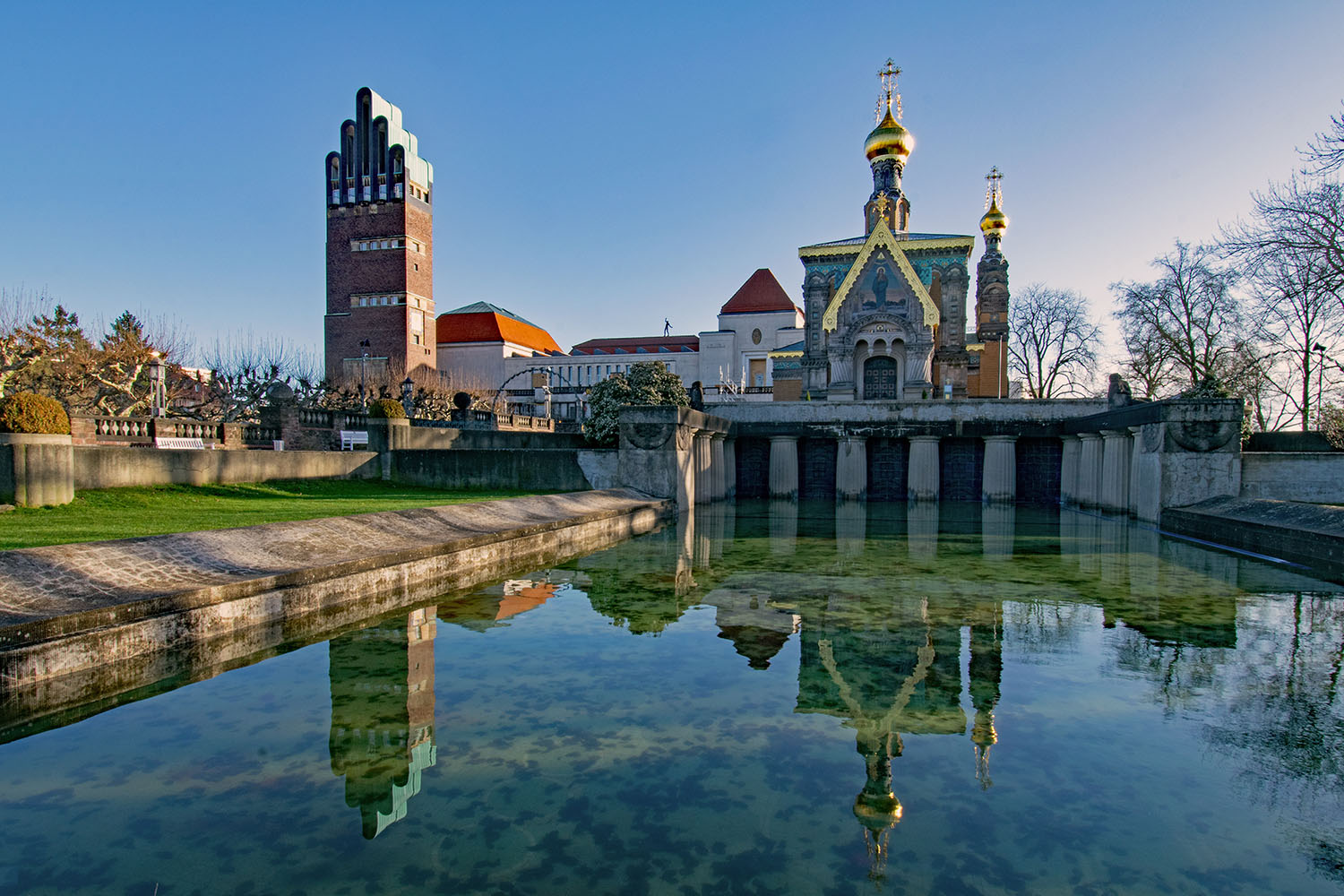 Blick auf das Russische Ensemble auf der Mathildenhöhe in Darmstadt mit der Russischen Kapelle und dem Hochzeitsturm, die sich im ruhigen Wasserbecken spiegeln.