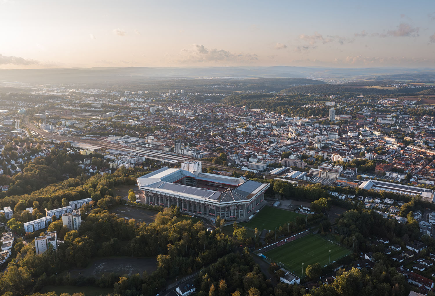 Luftaufnahme der Stadt Kaiserslautern mit dem Fritz Walter Stadion im Vordergrund, umgeben von Wohngebieten und Grünflächen.