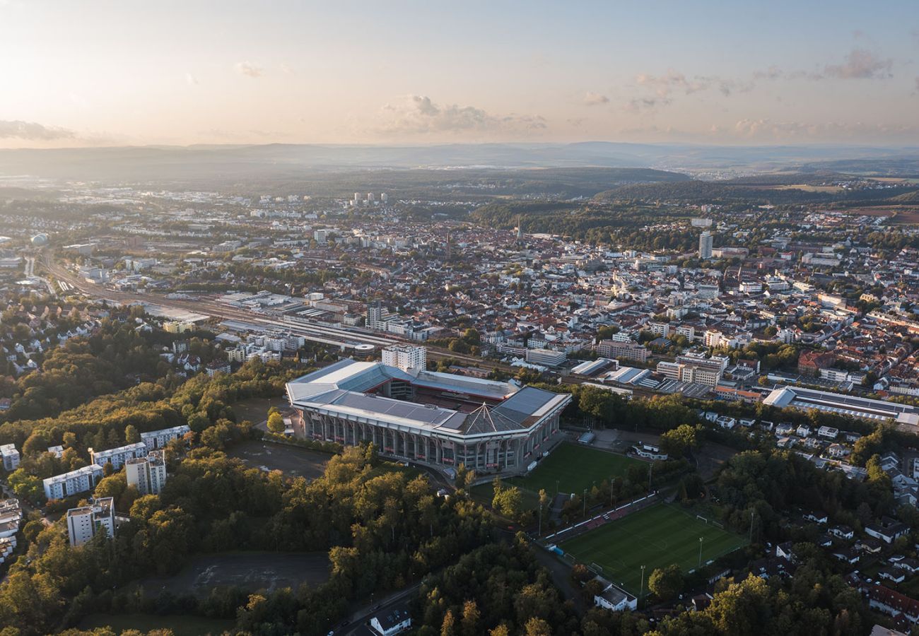 Luftaufnahme der Stadt Kaiserslautern mit dem Fritz Walter Stadion im Vordergrund, umgeben von Wohngebieten und Grünflächen.